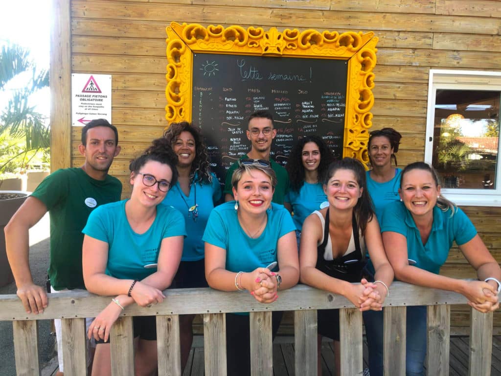 Équipe d'animation du camping Le Port de Moricq souriante devant le tableau du programme de la semaine