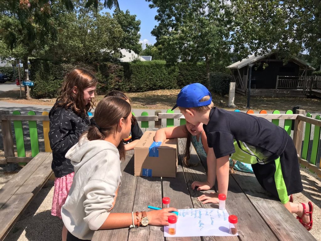 Enfants explorant des objets sur une table en extérieur.