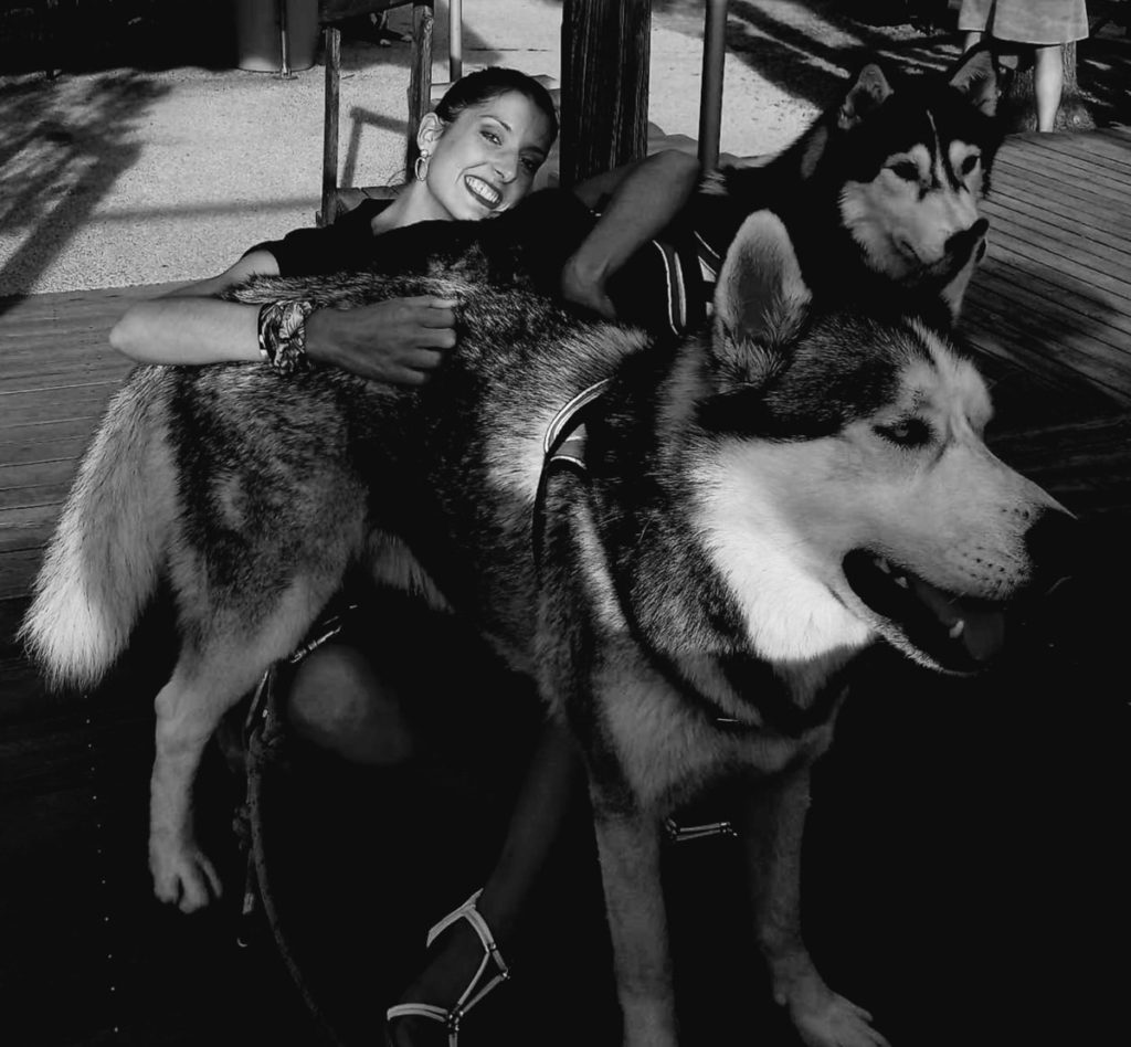 Femme souriante avec deux huskies affectueux sur terrasse.