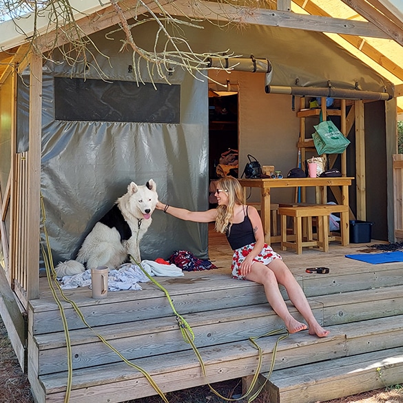 Femme caressant chien devant une tente de camping.