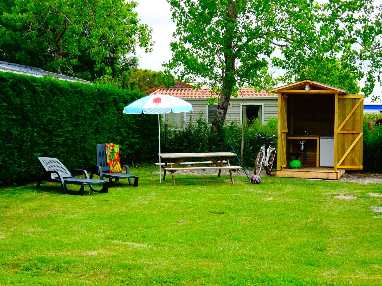 Emplacement camping avec table, chaises et parasol dans un jardin ombragé