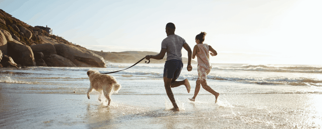 Couple courant avec chien sur la plage au coucher.