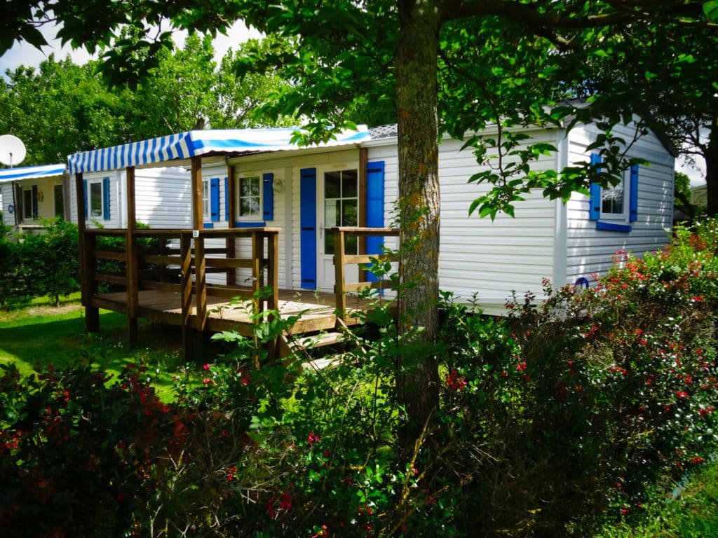 Mobil-home avec terrasse en bois et jardin fleuri.