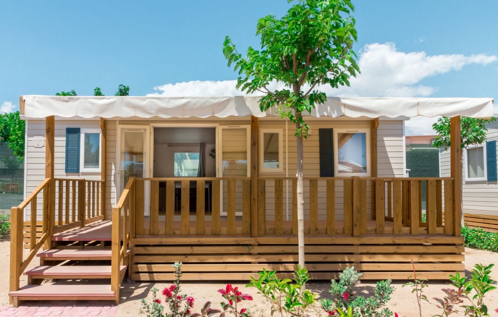 Mobil-home avec terrasse en bois et auvent blanc.