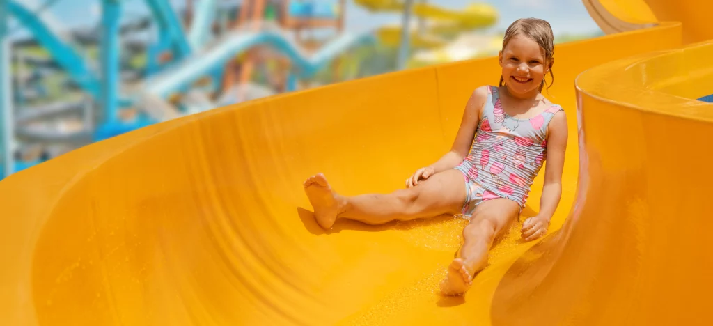 Enfant souriante sur un toboggan aquatique jaune.