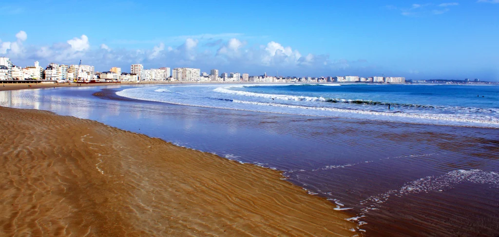 Plage ensoleillée avec vagues et immeubles en arrière-plan.