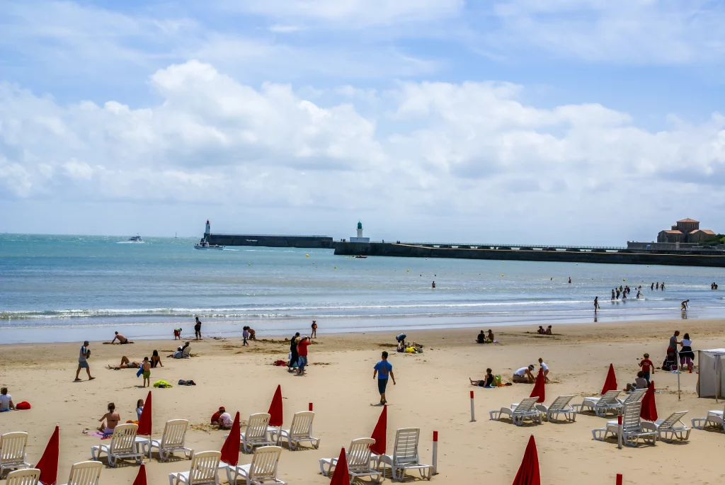 Plage animée avec parasols rouges et mer turquoise.