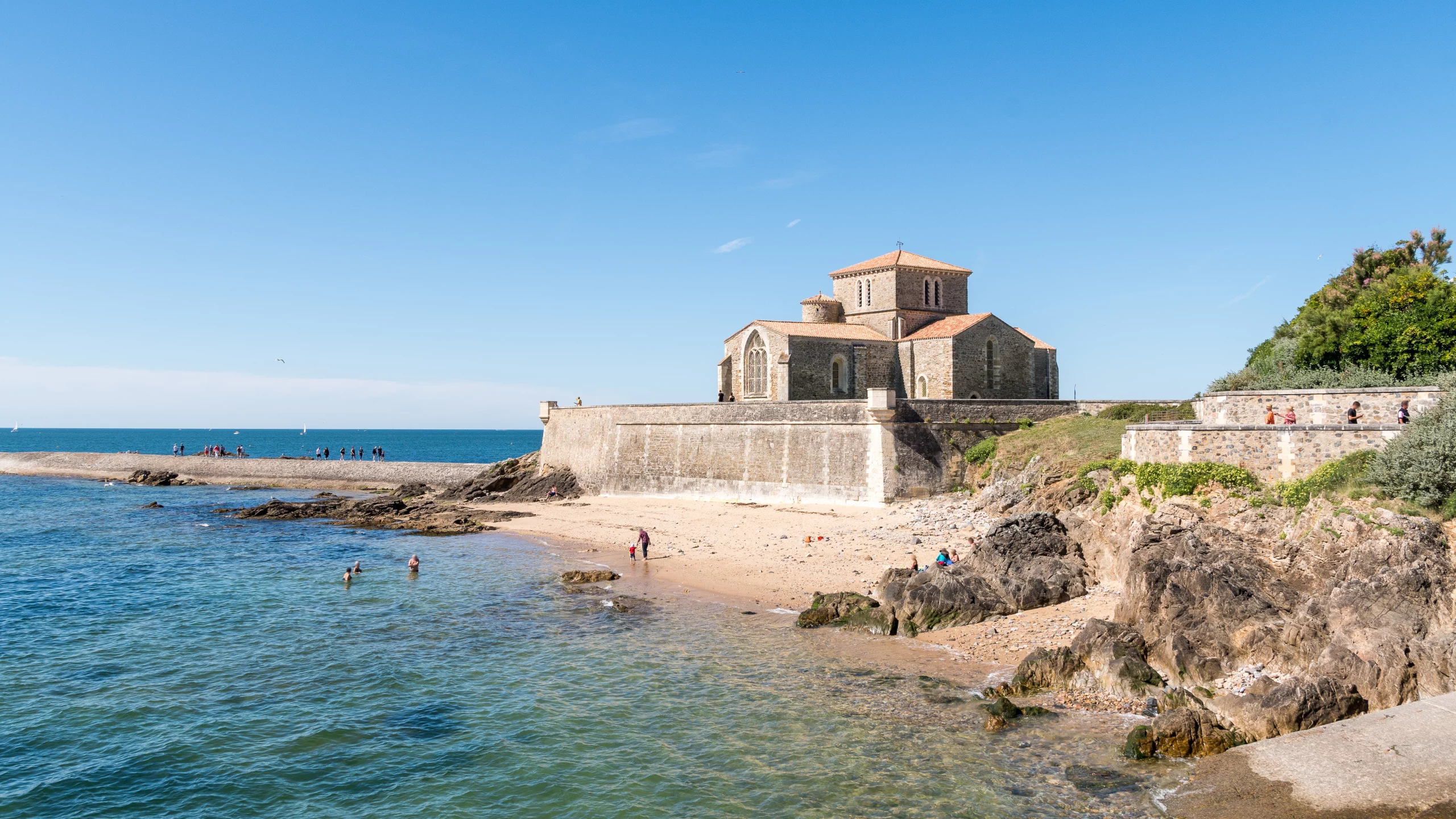 Chapelle romane sur plage, côte atlantique, ciel bleu.