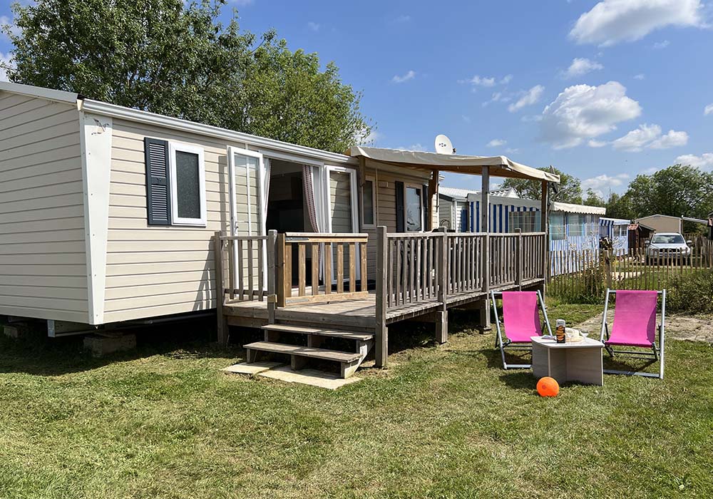 Mobil-home avec terrasse et chaises longues, journée ensoleillée.